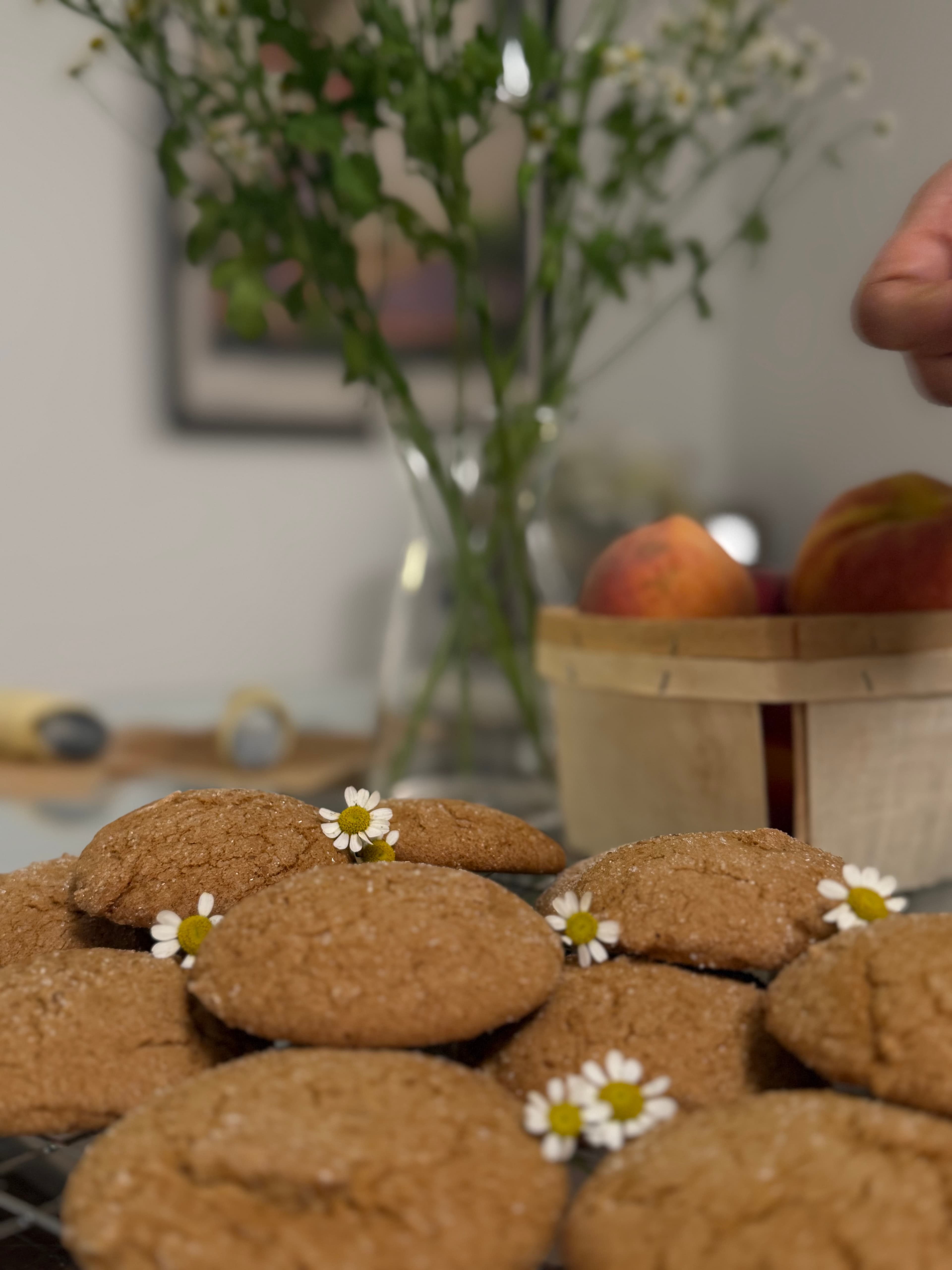A close-up of small-batch cookies fresh off the rack, tucked with chamomile blooms